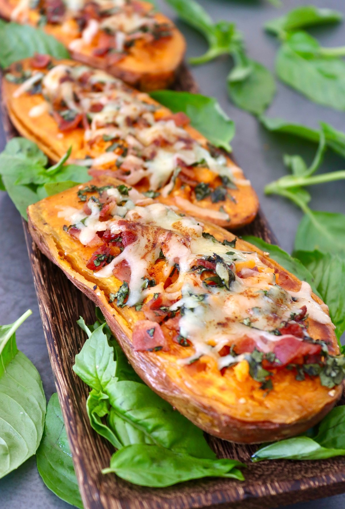 Three sweet potato halves topped with cheese, bacon and basil.