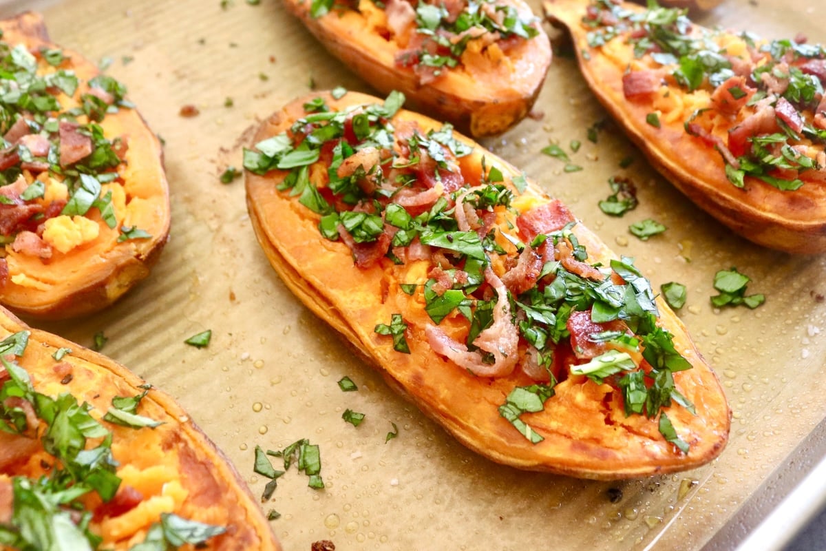 A few baked sweet potatoes halves with crumbled bacon and chopped basil on top.