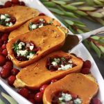 Several honeynut squash with cranberry, spinach and onion filling, with dots of roquefort cheese on top, on a white platter.