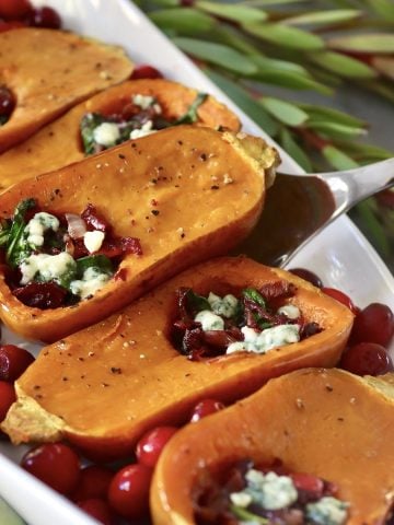 Several honeynut squash with cranberry, spinach and onion filling, with dots of roquefort cheese on top, on a white platter.
