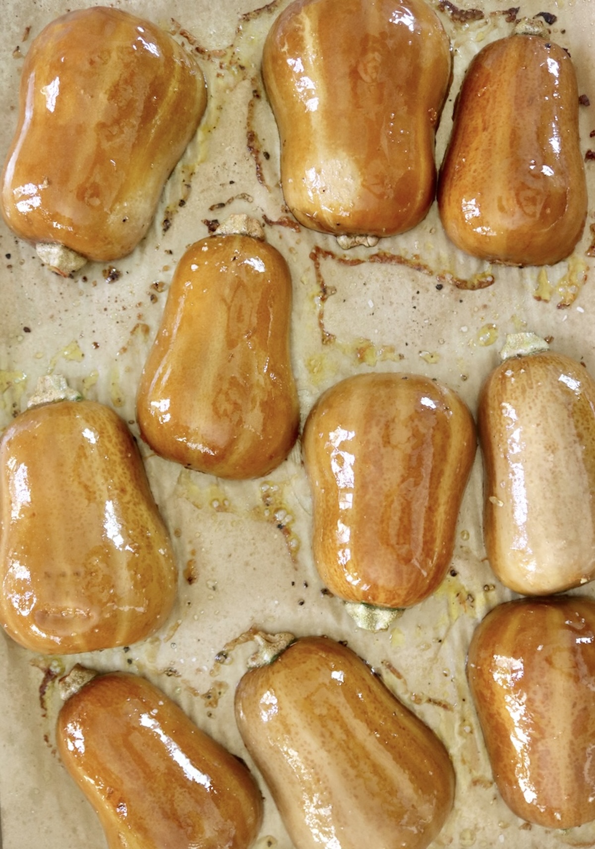 Several halved and baked honeynut squash, round side up, on a a prchment-lined sheet pan.