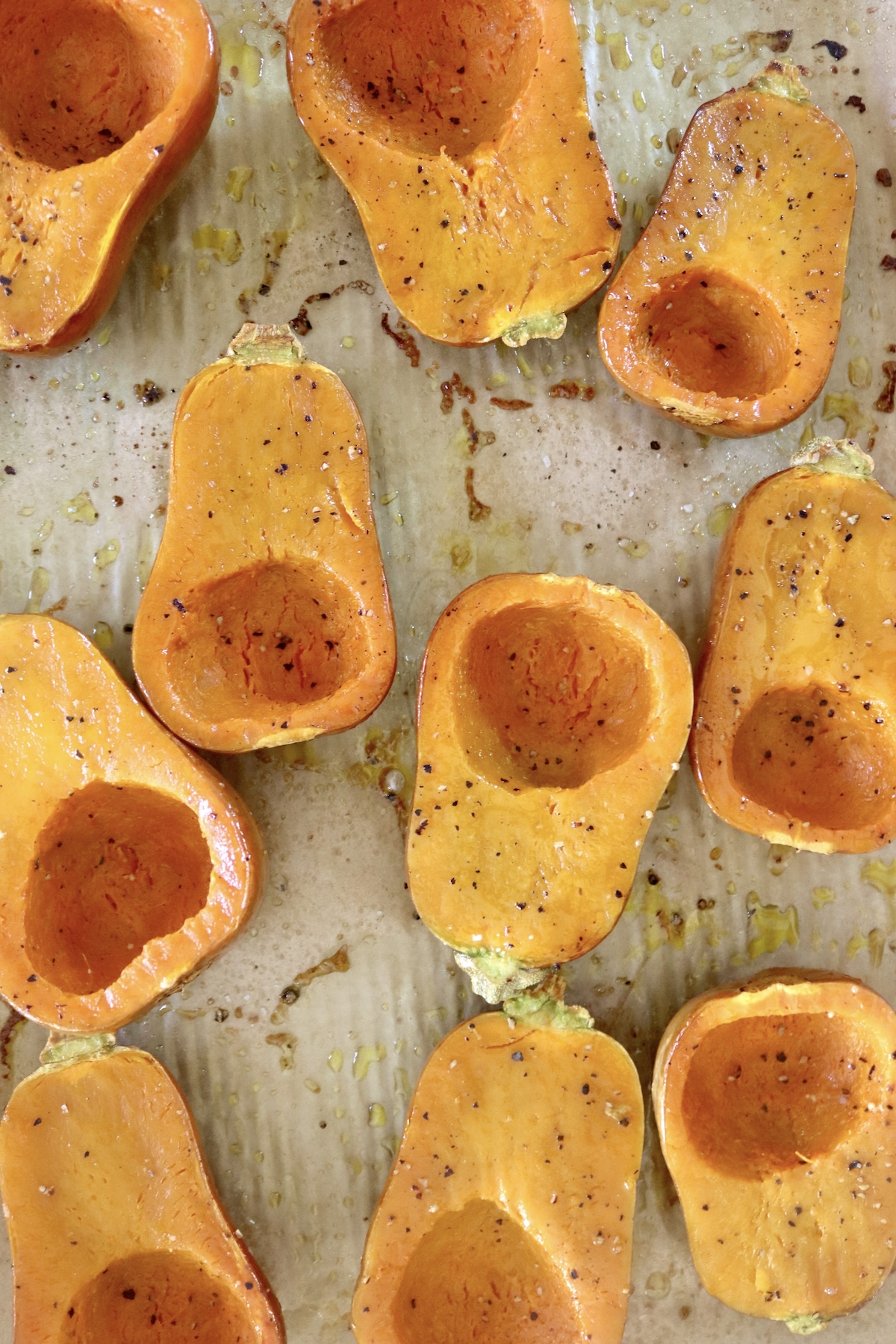 Several halved and baked honeynut squash, round side down, on a a prchment-lined sheet pan.
