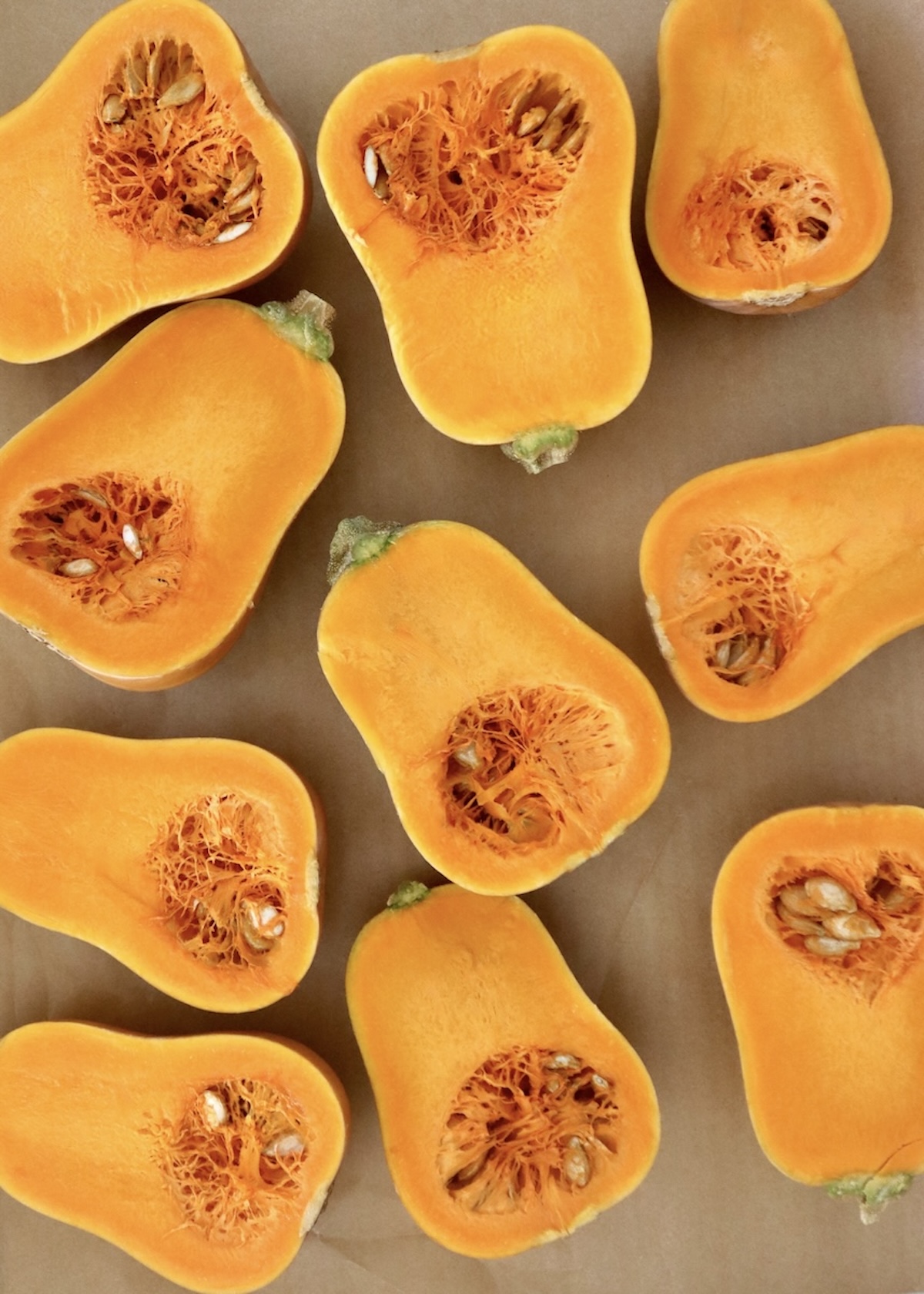 Several raw, halved honeynut squash, round side down, on a a prchment-lined sheet pan.