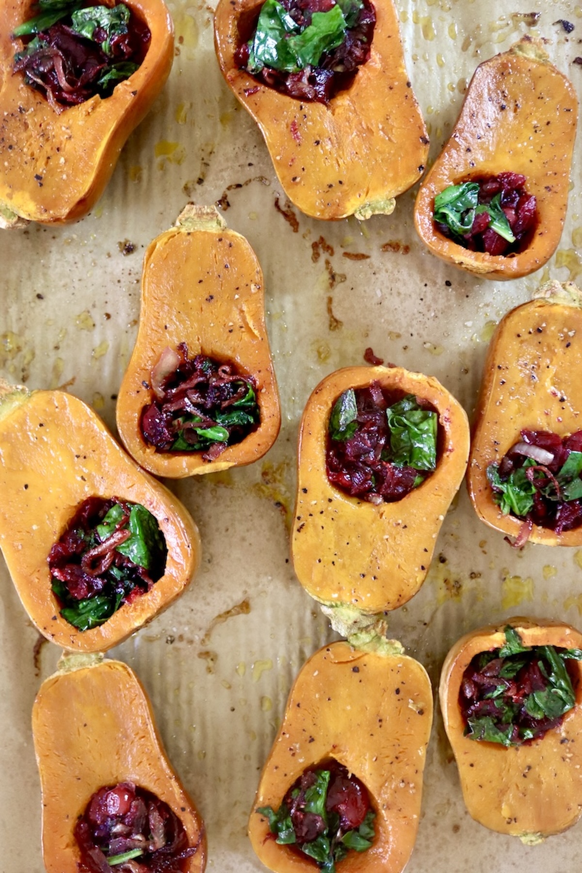 Several halved and baked honeynut squash filled with cranberries and spinach, on a a prchment-lined sheet pan.