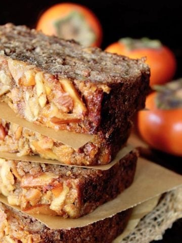 Four stacked slices of persimmon cake with three whole persimmons behind it.