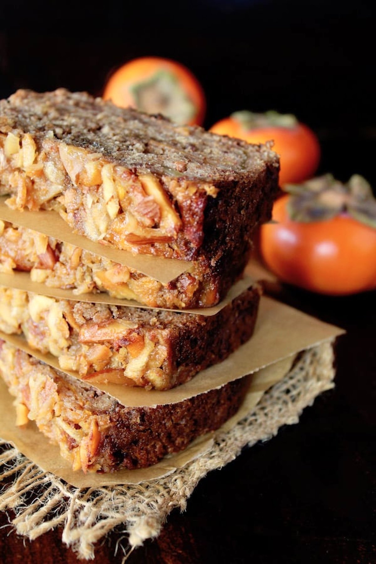 Four stacked slices of persimmon cake with three whole persimmons behind it.
