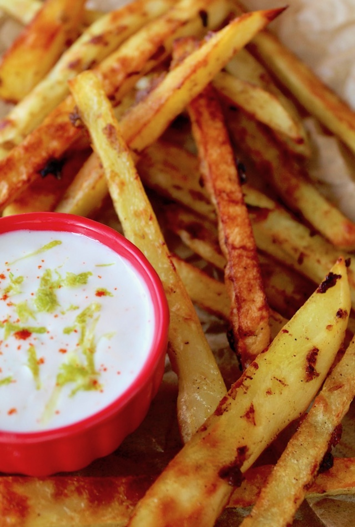 Curry fries with yogurt dip in a tiny red bowl with lime zest on top.