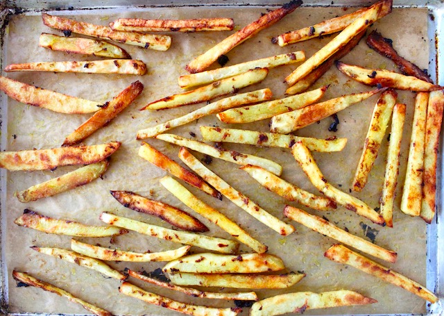 Cooked potato sticks on a sheet pan with curry paste.