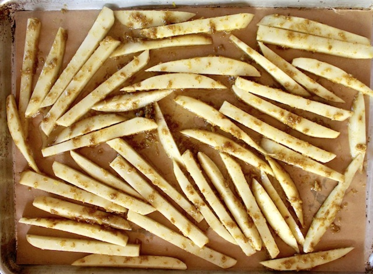 Raw potato sticks on a sheet pan with curry paste.
