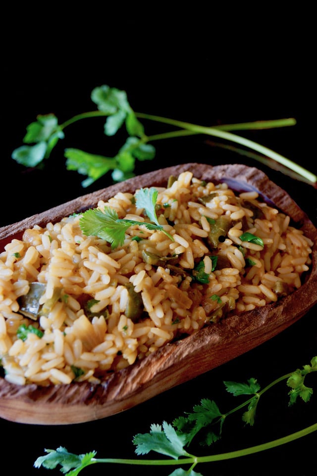 Mexican Poblano Rice Pliaf in a wooden, oval-shpaed bowl with cilantro sprigs.