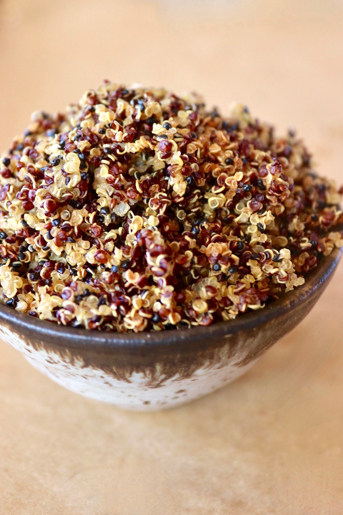 Side view of a tiny ceramic bowl filled with multi-colored quinoa crispy.