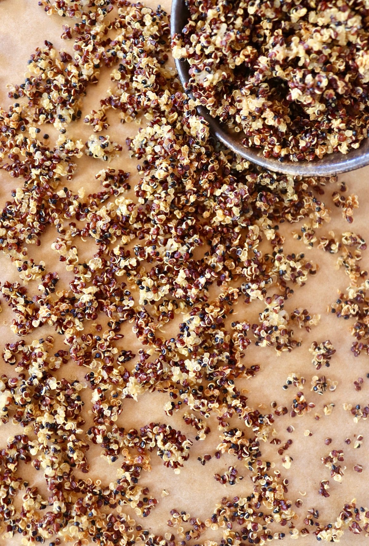 Crispy quinoa spilling out of a small ceramic bowl on parchment paper.