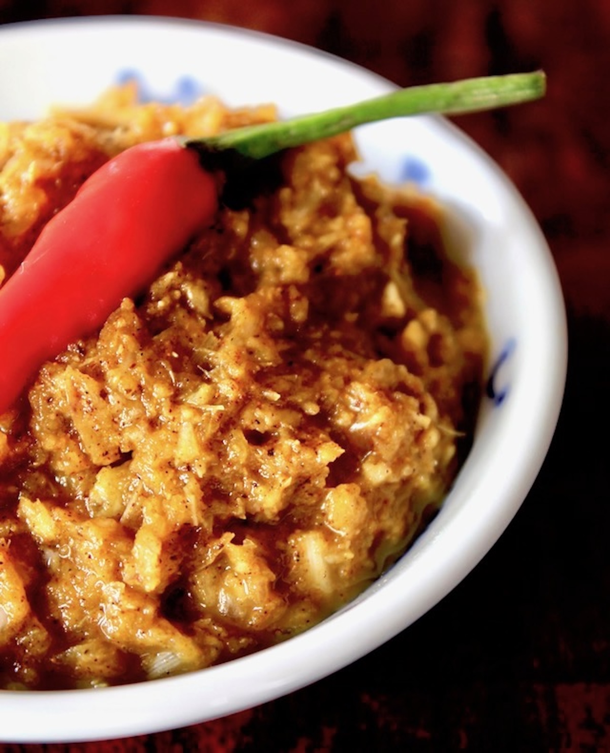 Yellow curry paste in a white bowl with a red thai chili on top.