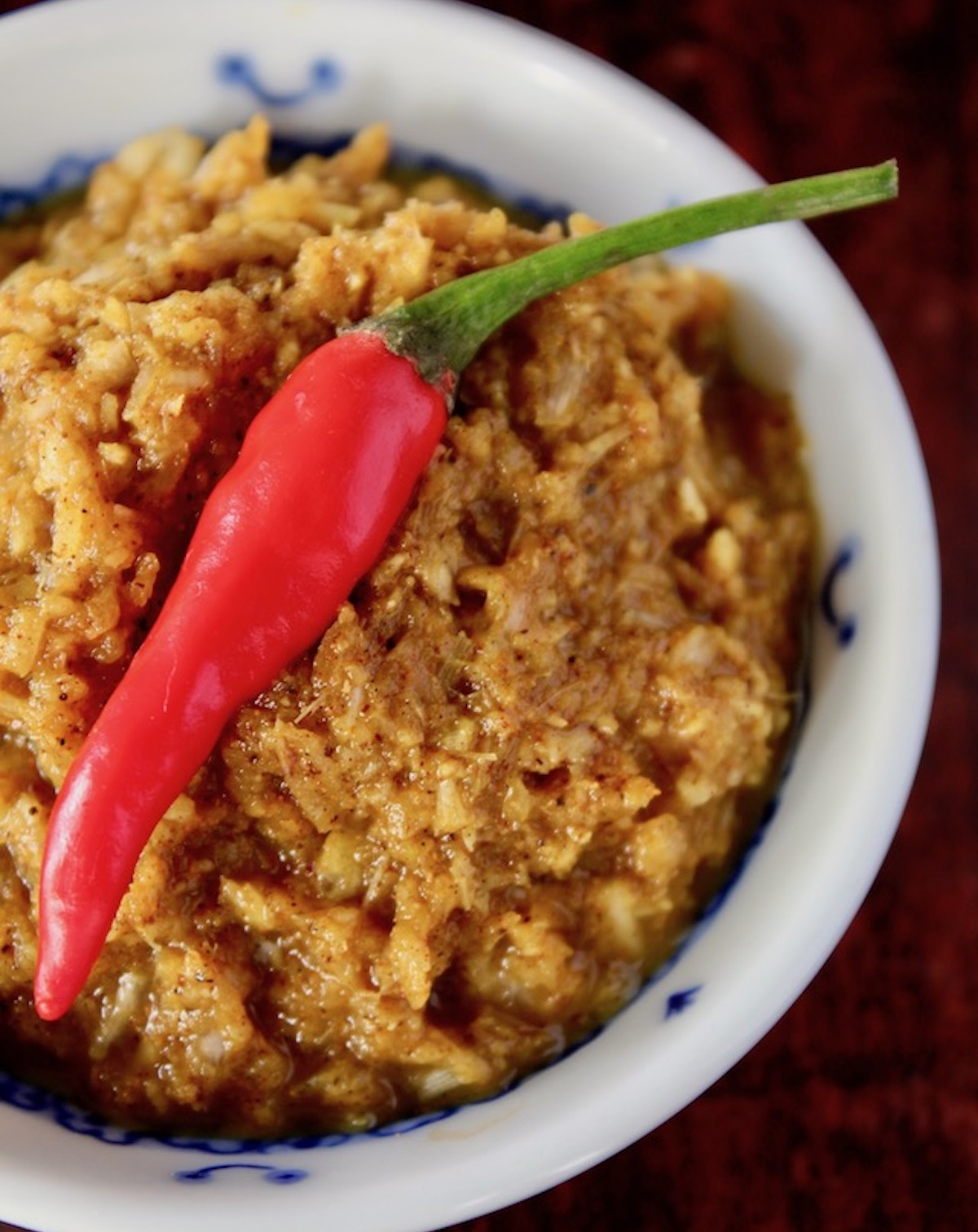 Yellow curry paste in a small white bowl with one red pepper on top.