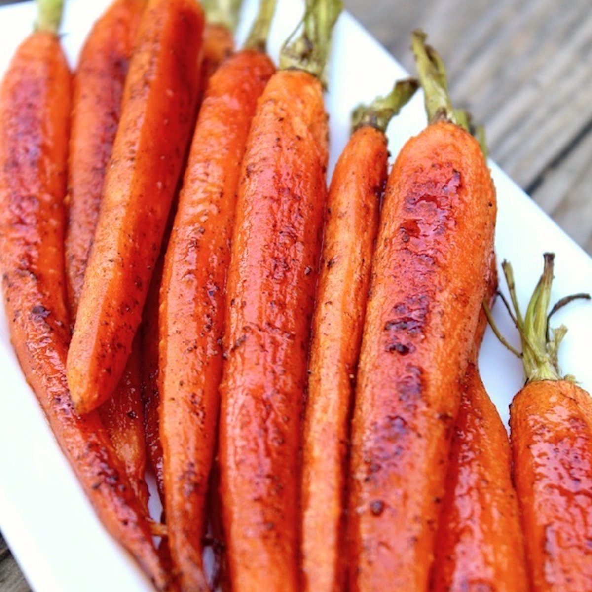 White rectangular plate filled with baby roasted carrots, with stems still on.
