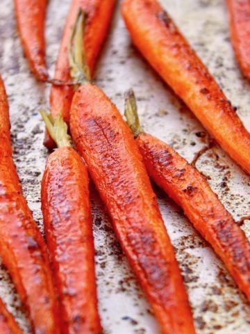 Roasted, glazed baby carrots with stems on, on a sheet pan.