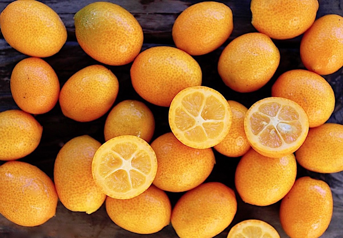 Kumquat-Marmalade Dozens of fresh kumquats on a wood surface - a few are sliced.