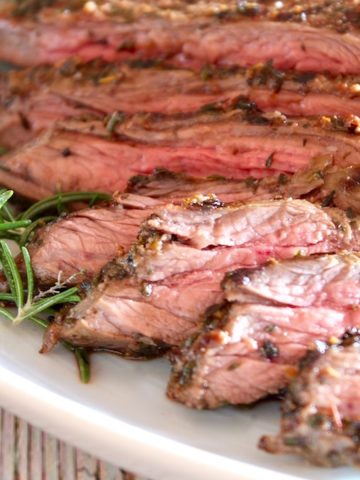 sliced mediterranean marinated steak with fresh rosemary on white platter