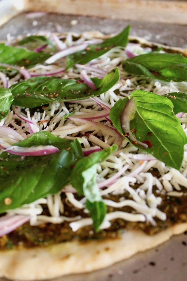 Green pizza with mozzarella and basil leaves ready for the oven