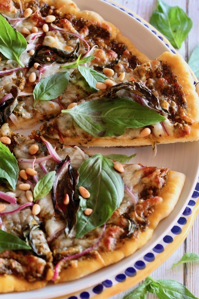 Basil Pizza with one slice being taken out on yellow-rimmed plate.