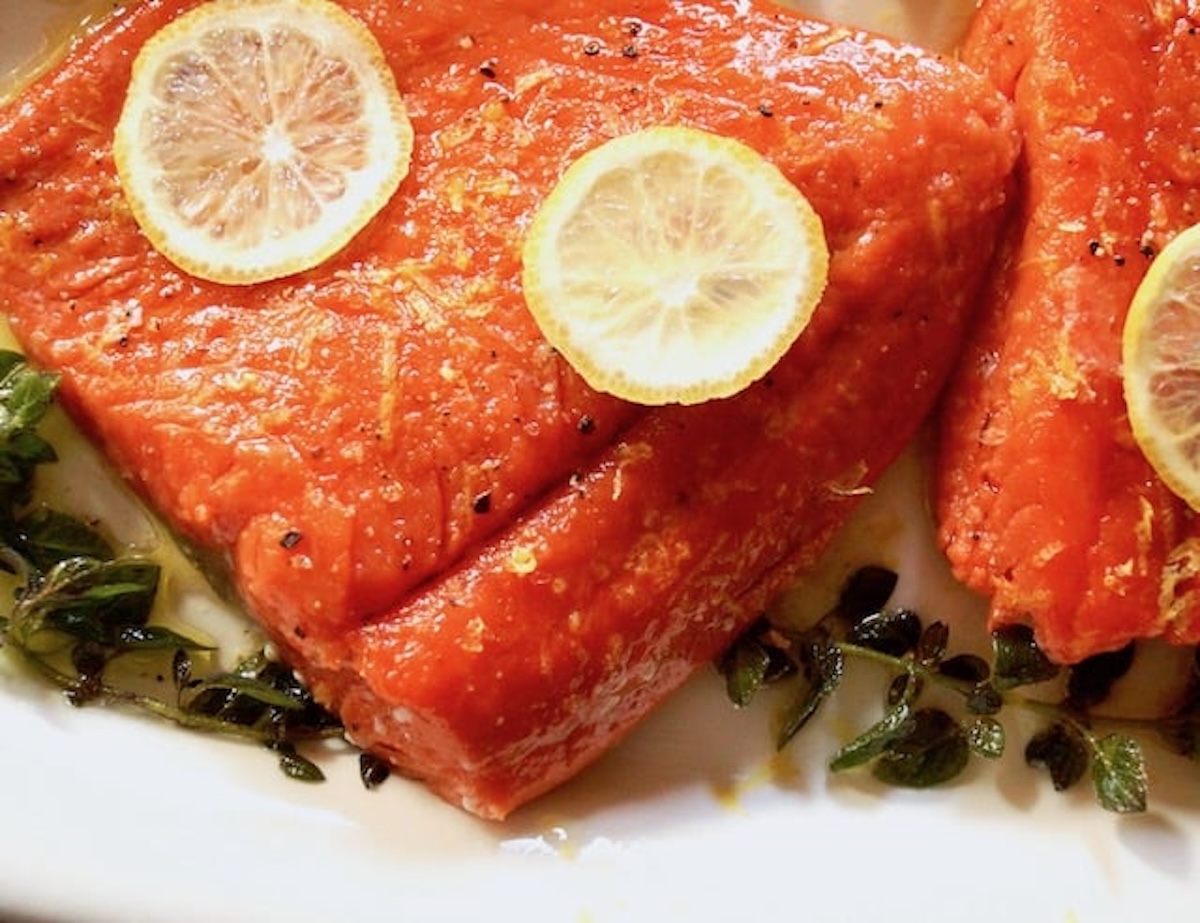 One fillet of Olive Oil Poached Fish (Salmon) on a white platter with lemon.