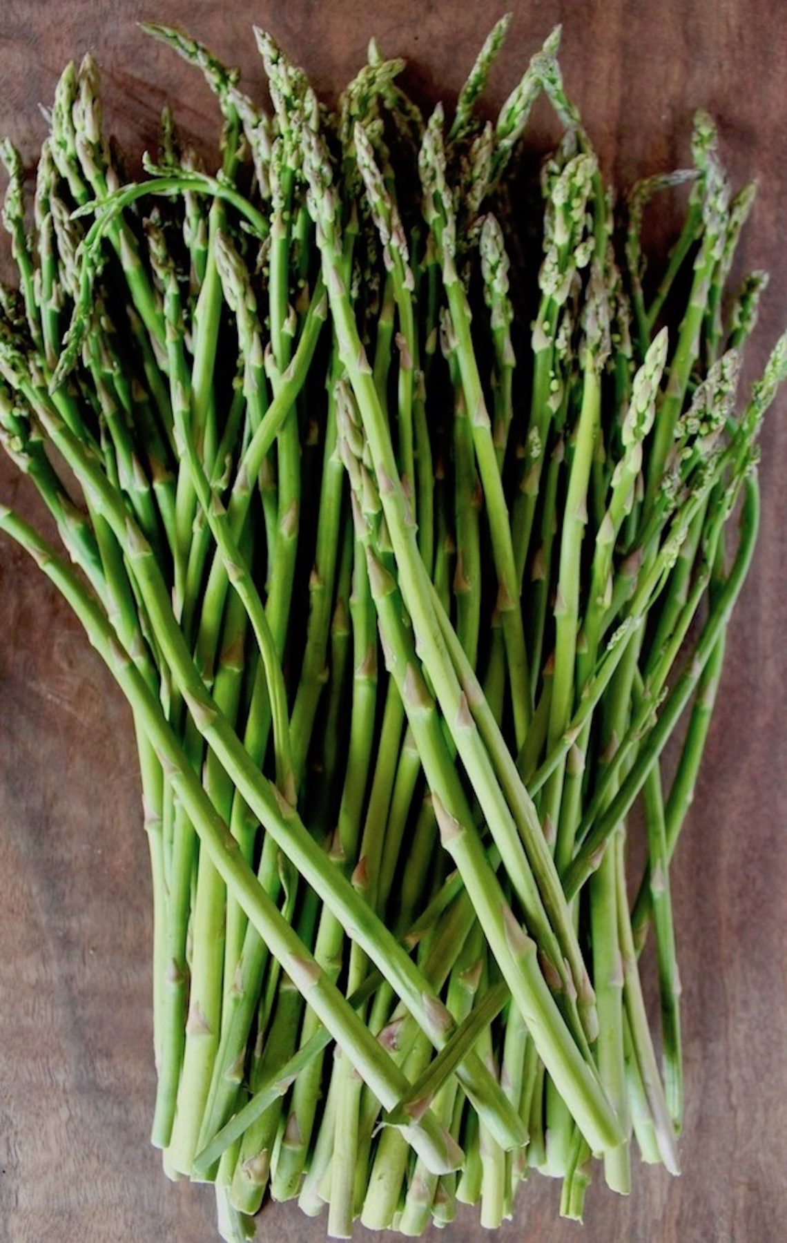 Beautiful skinny asparagus spears on dark wood cutting board .