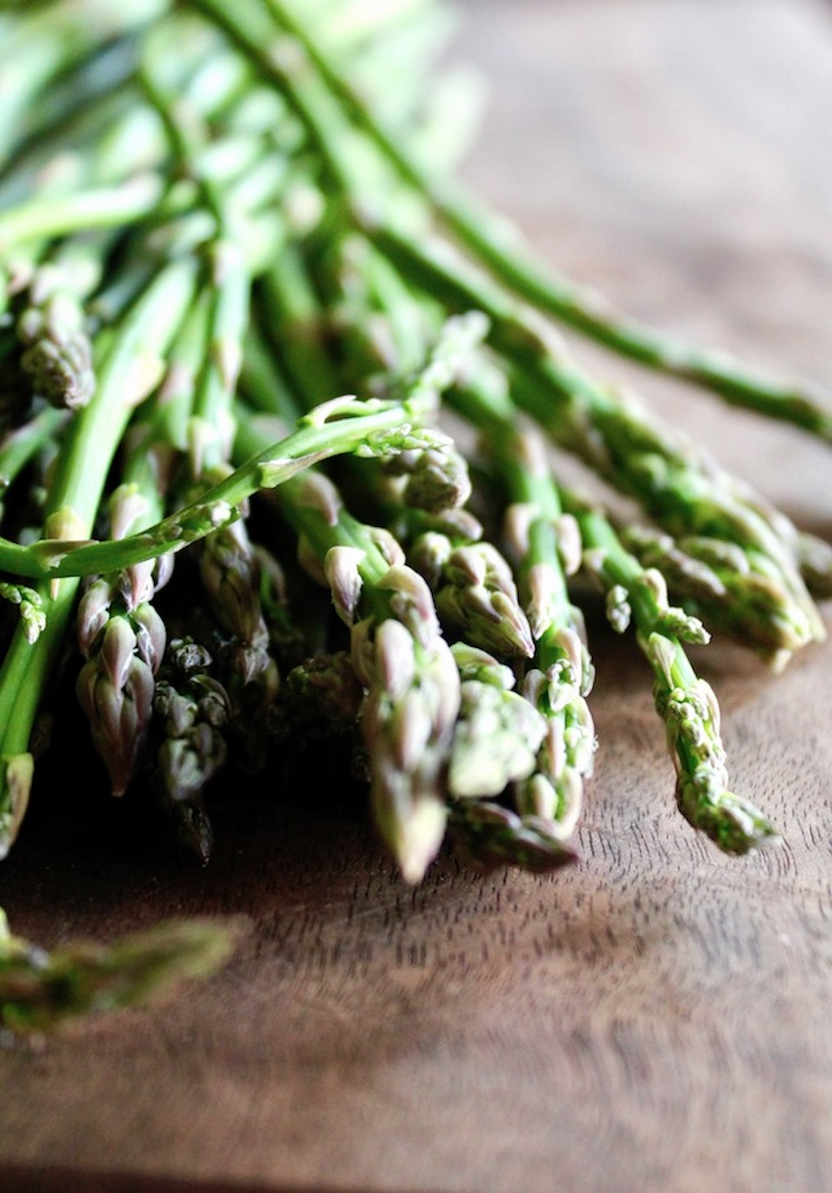 Beautiful skinny asparagus spears on dark wood cutting board with a close up of the tips.