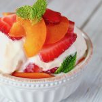Minty strawberries and apricots over vanilla ice cream in white bowl.