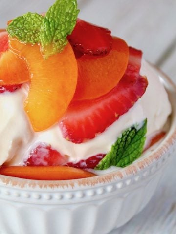 Minty strawberries and apricots over vanilla ice cream in white bowl.