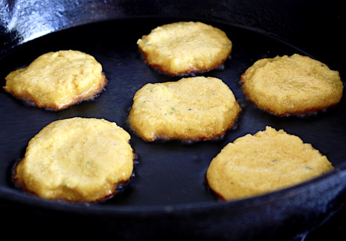 5 round hot water cornbreads in a skillet, partially cooked (looks like pancakes.)