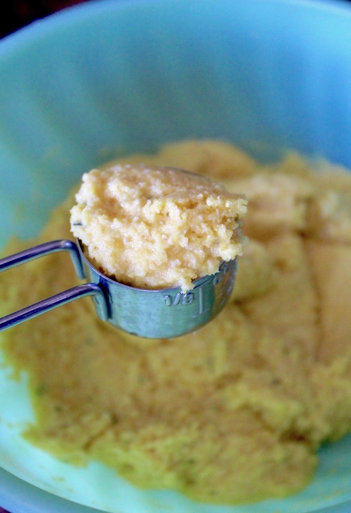Green bowl with cornbread batter with a small scoop of it over the bowl.