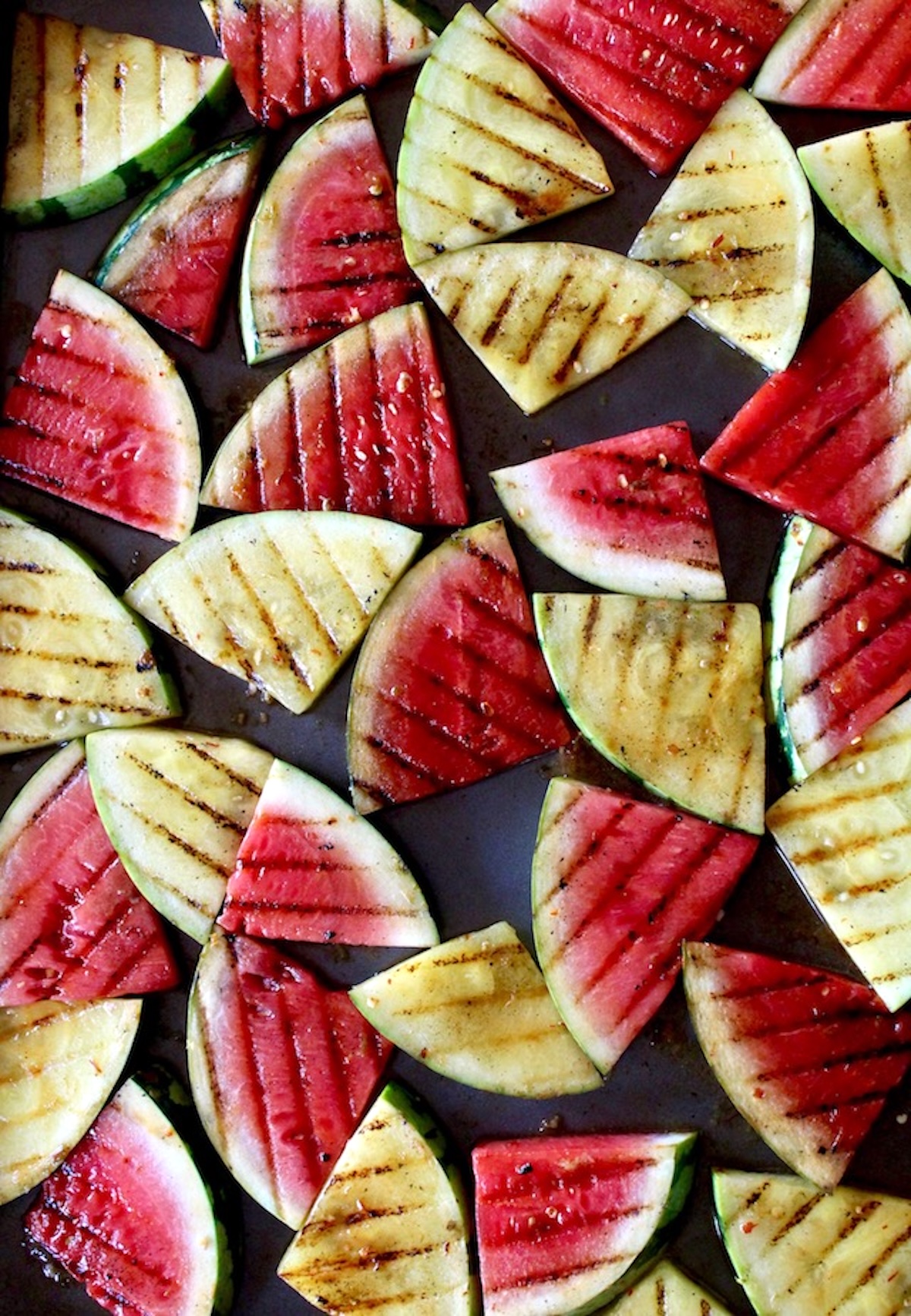 Lime-Chile-Grilled-Watermelon Dozens of small grilled triangular watermelon slices with lime on a sheet pan.