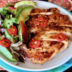 sliced tequila lime chicken on white plate with a side salad