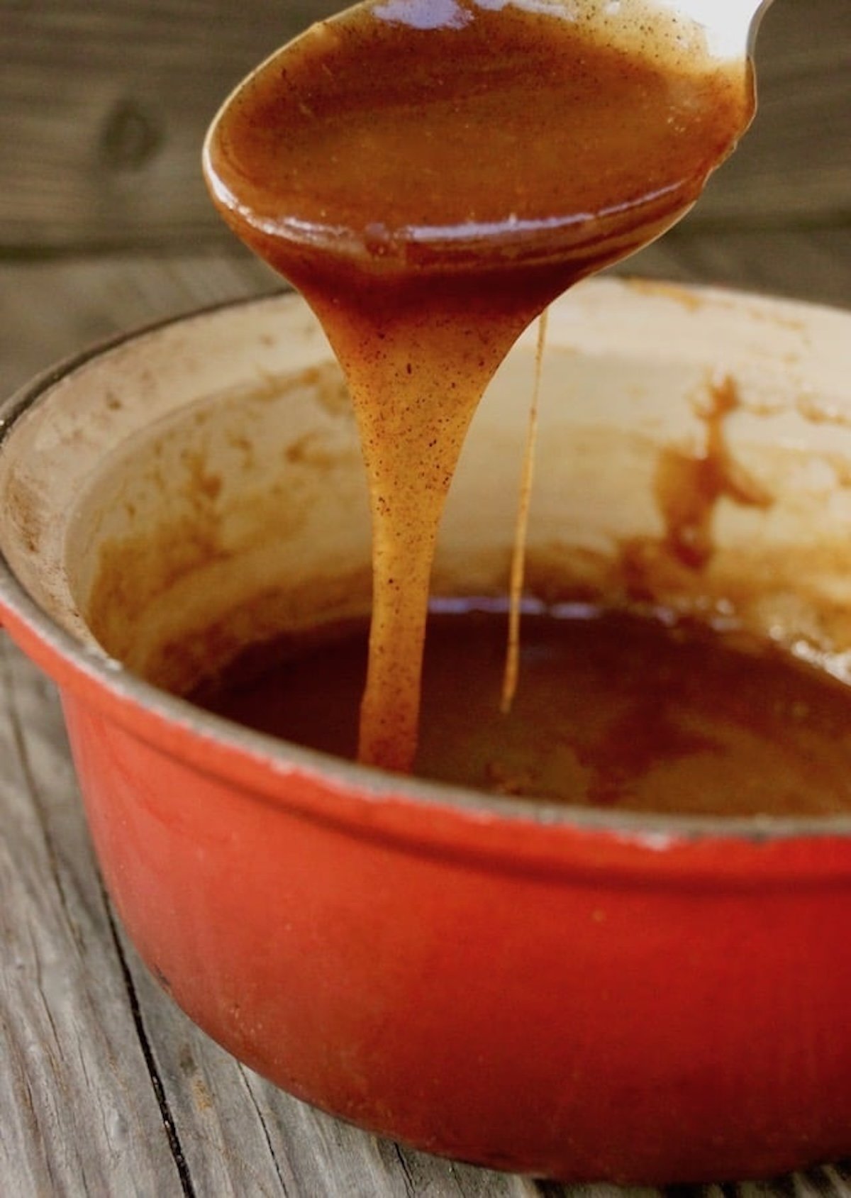 Spiced caramel sauce dripping off a spoon into a red pot.