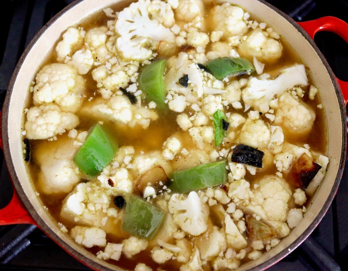 Pot filled with vegetable stock, cauliflower and green pepeprs.