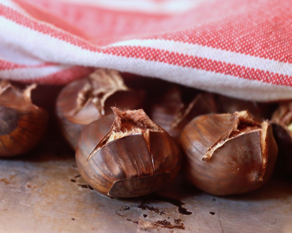 A few roasted chestnuts peeking out from under a red kitchen towel.