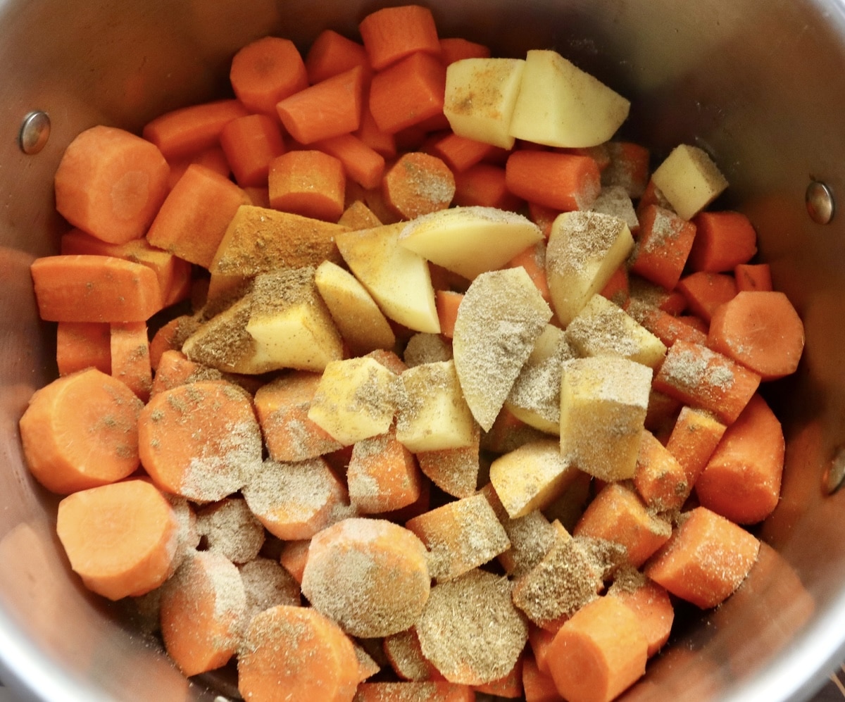 Coconut-Spiced-Carrot-Soup Raw, chopped carrots and potatoes with cardamom, cumin and turmeric sprinkled on top.