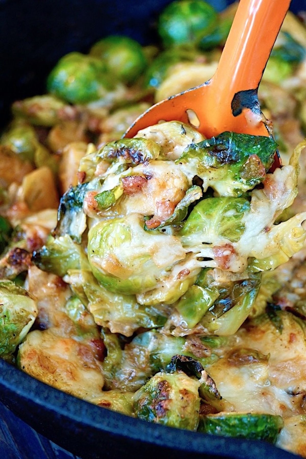 Cheesy brussels sprouts baked with pancetta, with a big orange spoon holding some of it up.