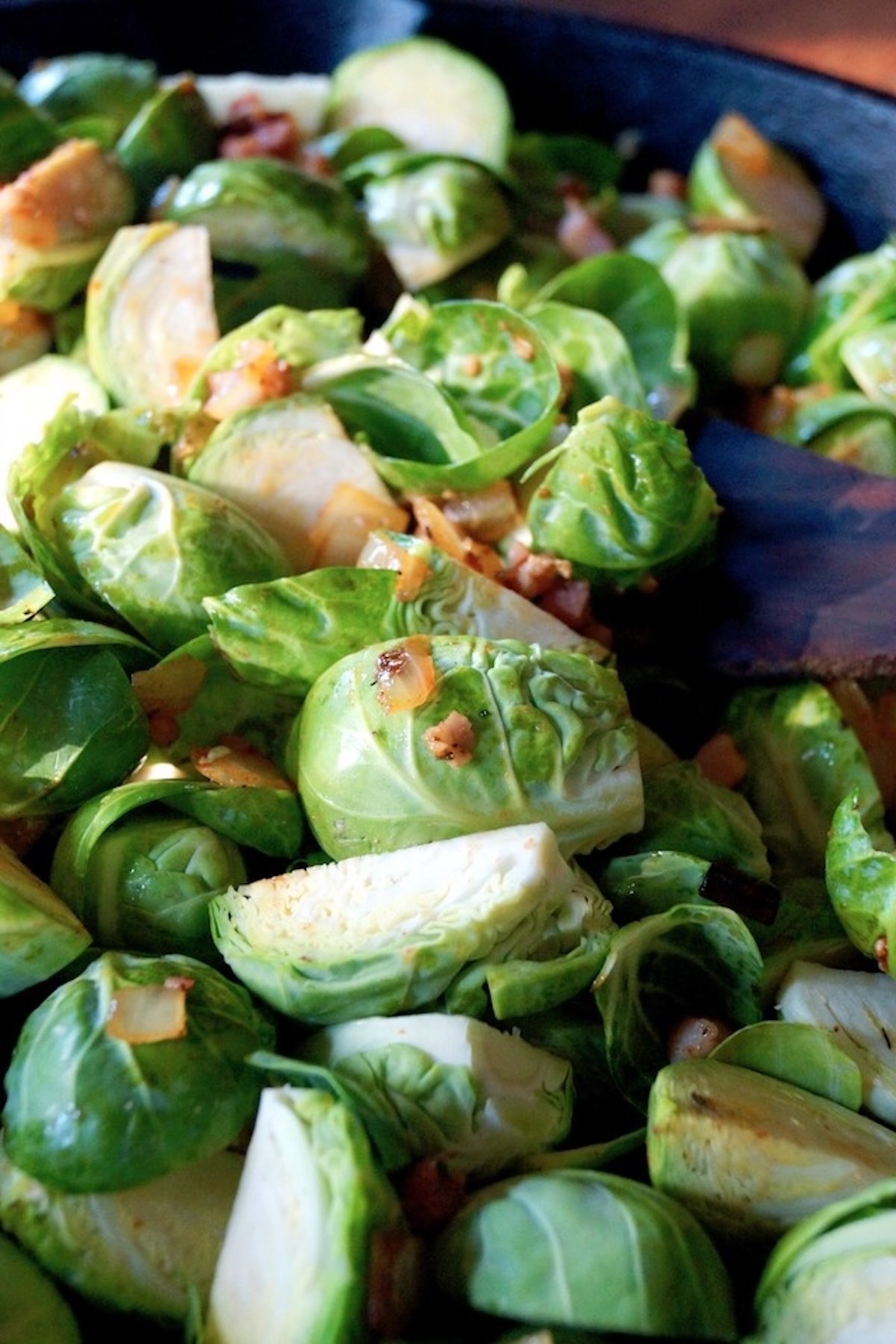 Raw halved brussels sprouts in a pan with bits of pancetta.