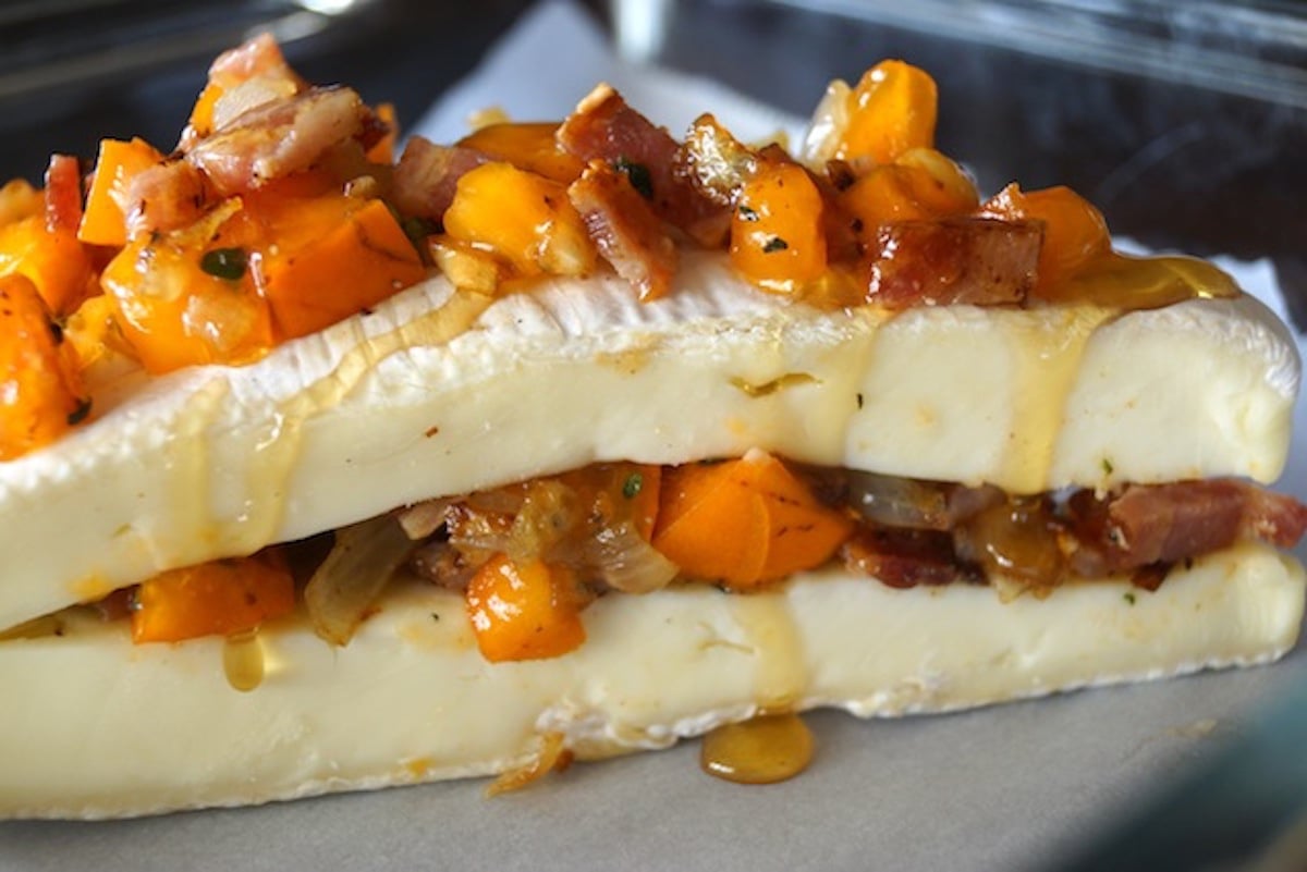 Wedge of brie cheese sliced in half horizontally with persimmon-onion mixture inside and on top.