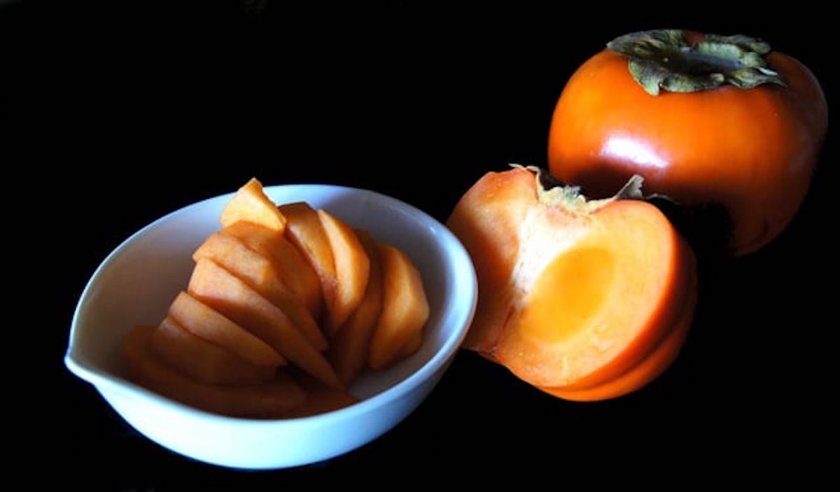 Sliced Fuyu persimmon is a white bowl with one persimmon cut in half.