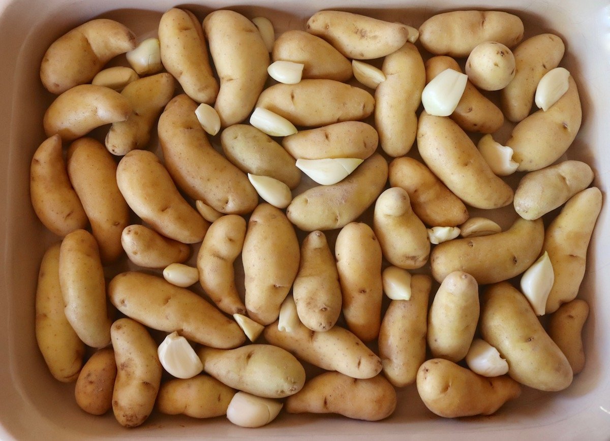 fingerling potatoes in a casserole dish with raw garlic pieces.