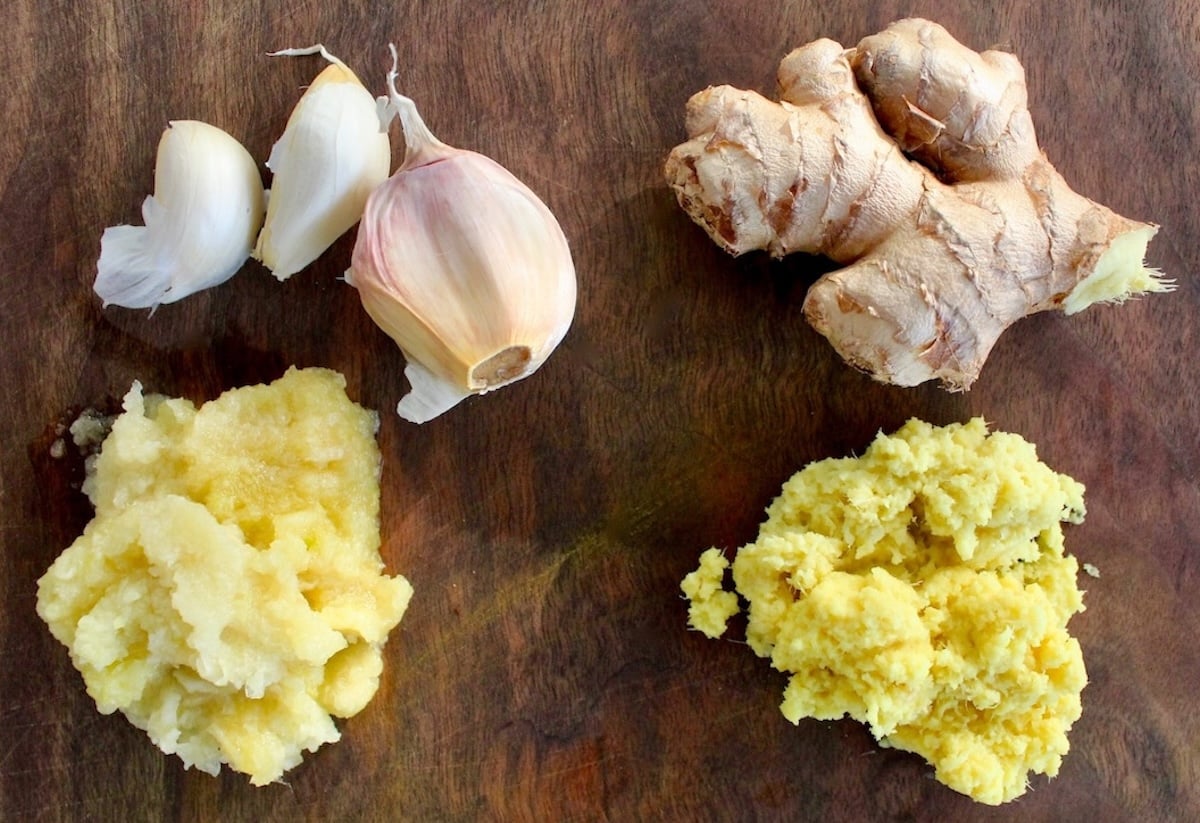 Ginger and garlic pulp on cutting board with garlic cloves and ginger finger.