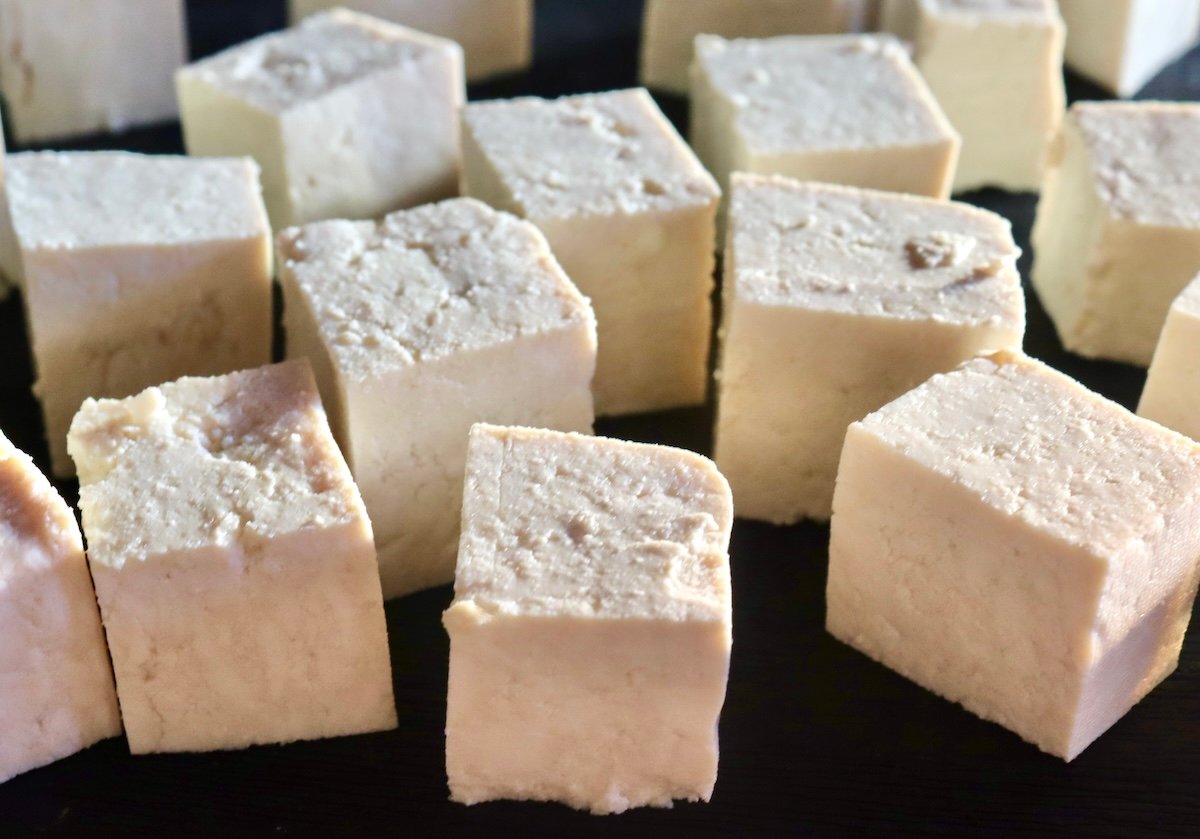 Cubed raw tofu on a black cutting board.