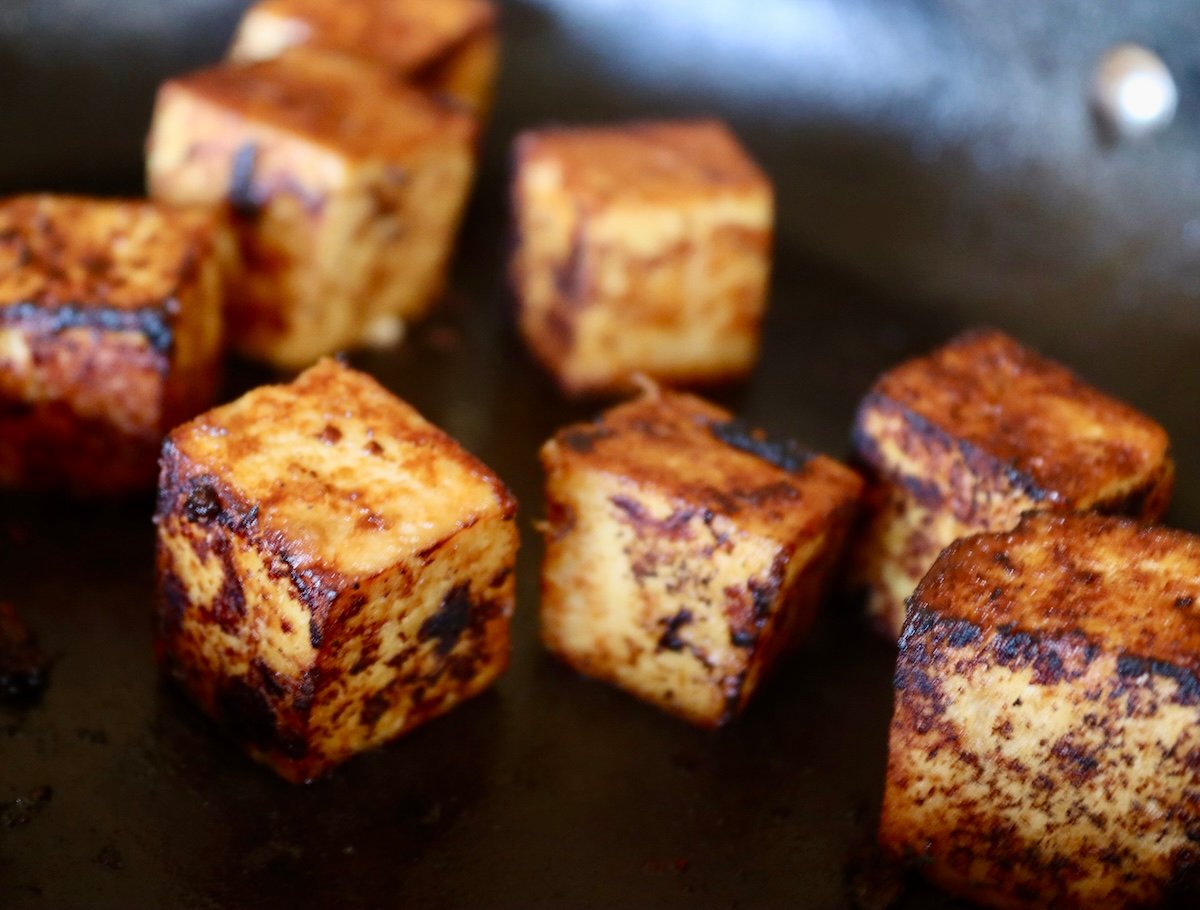 Super seared and golden cubes of marinated tofu in skillet.