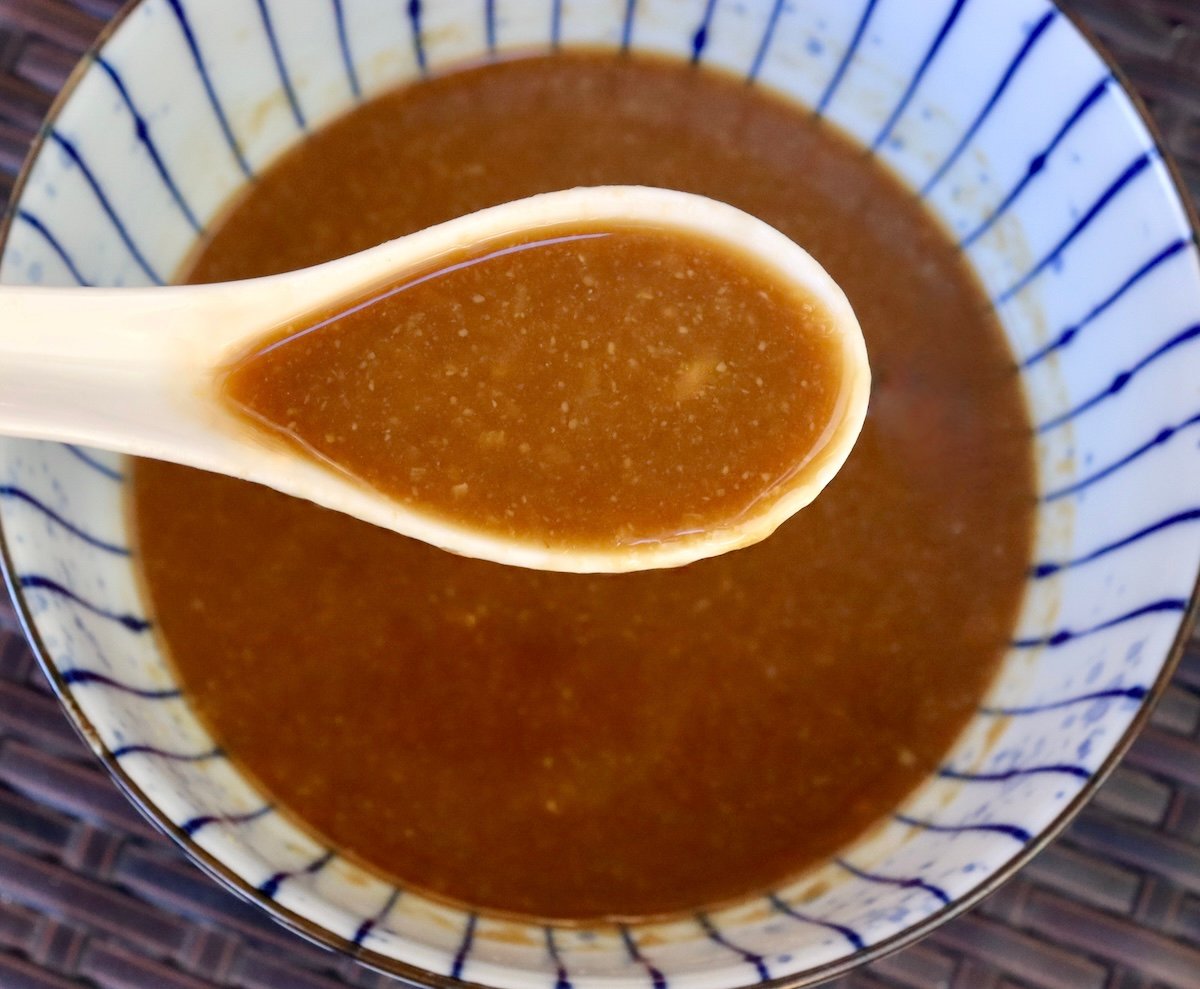 Small ceramic bowl with blue stripes with an Asian miso sauce and a white soup spoon.