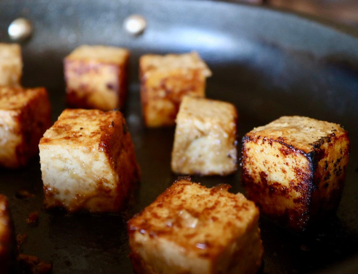 Partially seared and golden cubes of marinated tofu in skillet.