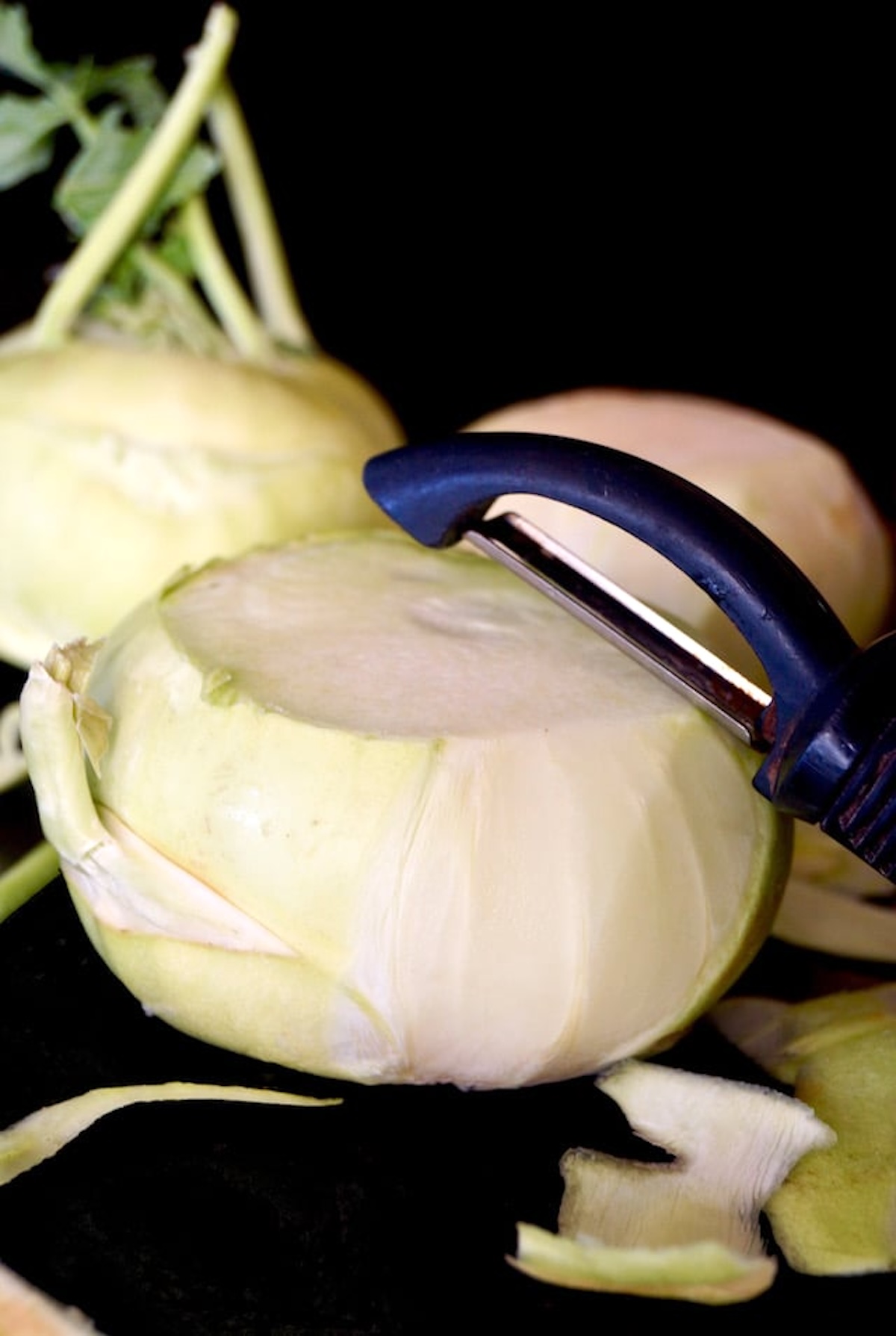 Whole kohlrabi being peeled with vegetable peeler.