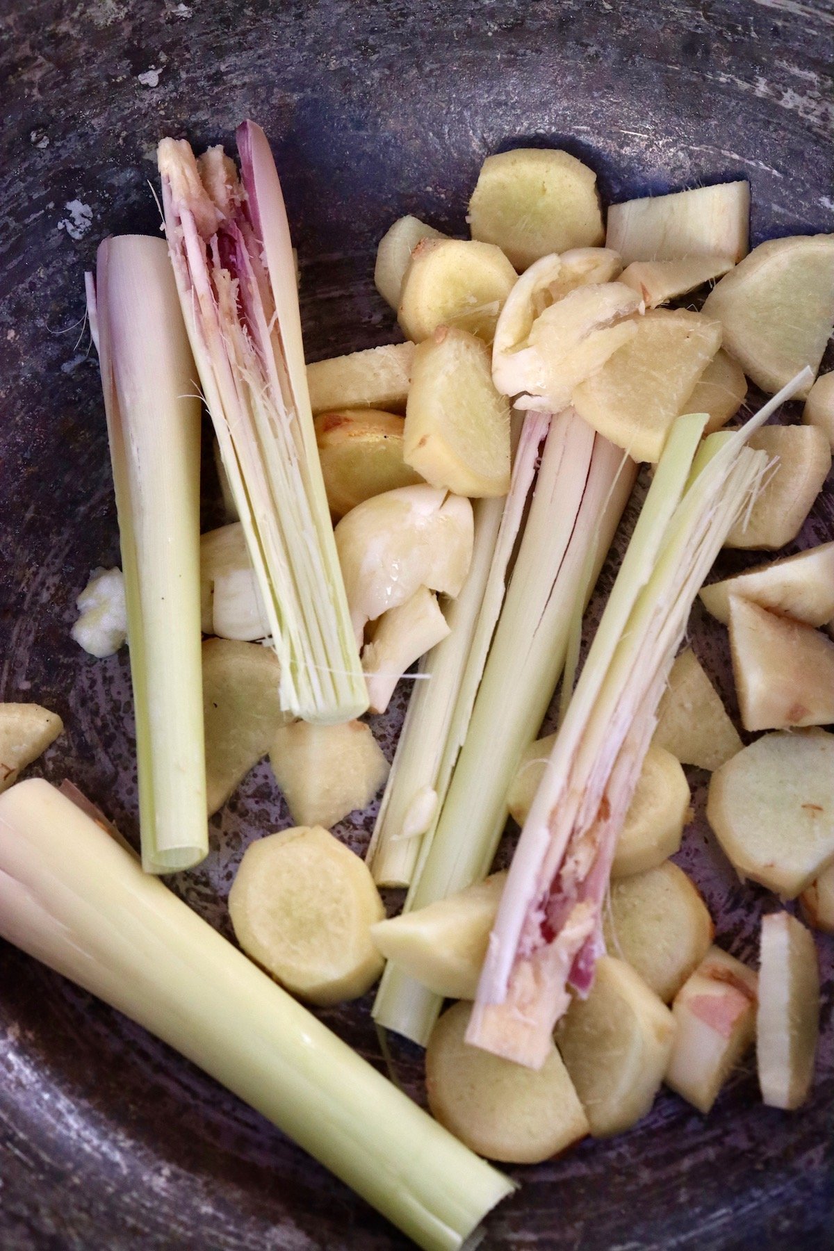 bottom of a pot with pieces of ginger, lemongrass and garlic