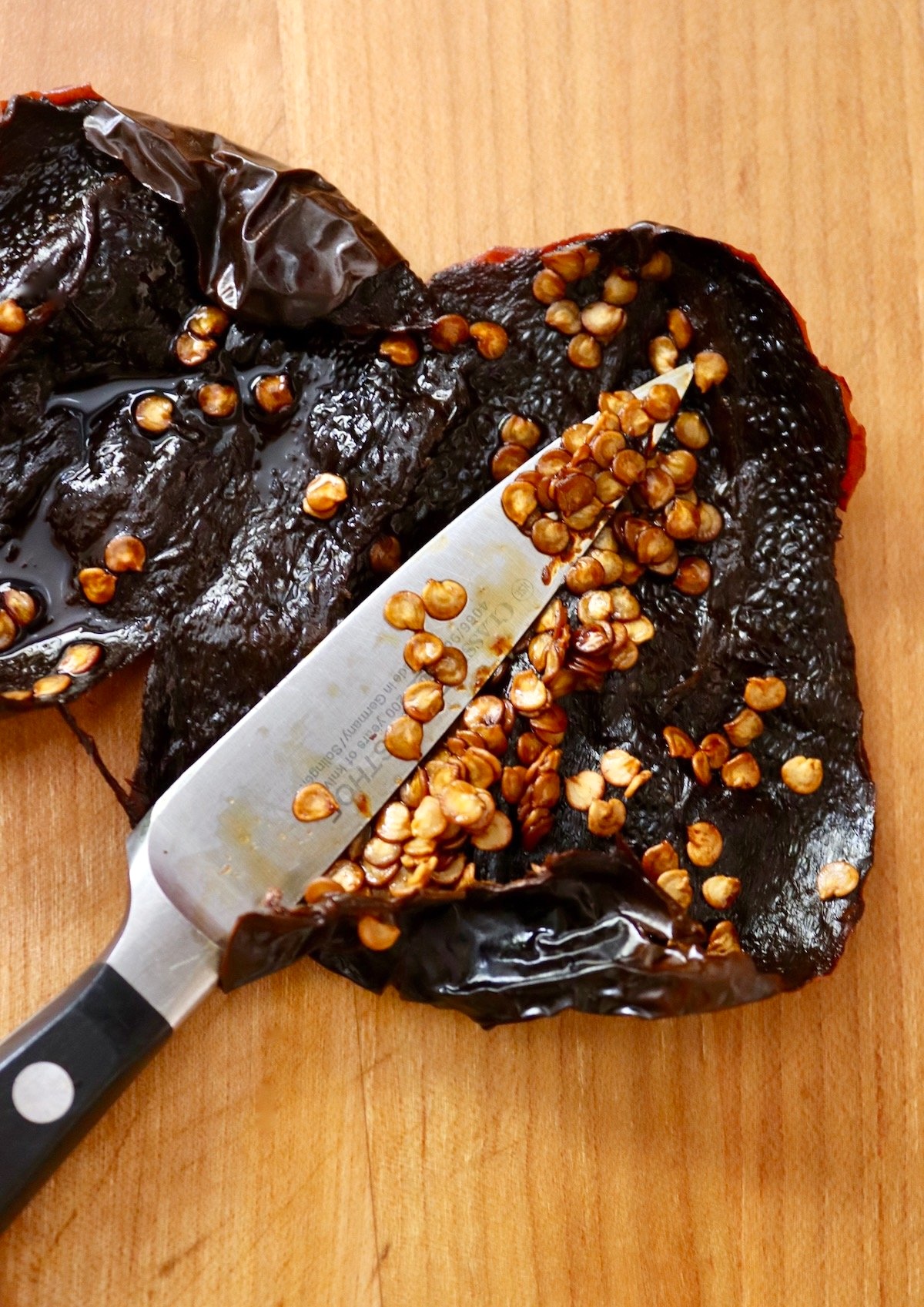 Hydrated ancho chiles with seeds being removed with a paring knife.